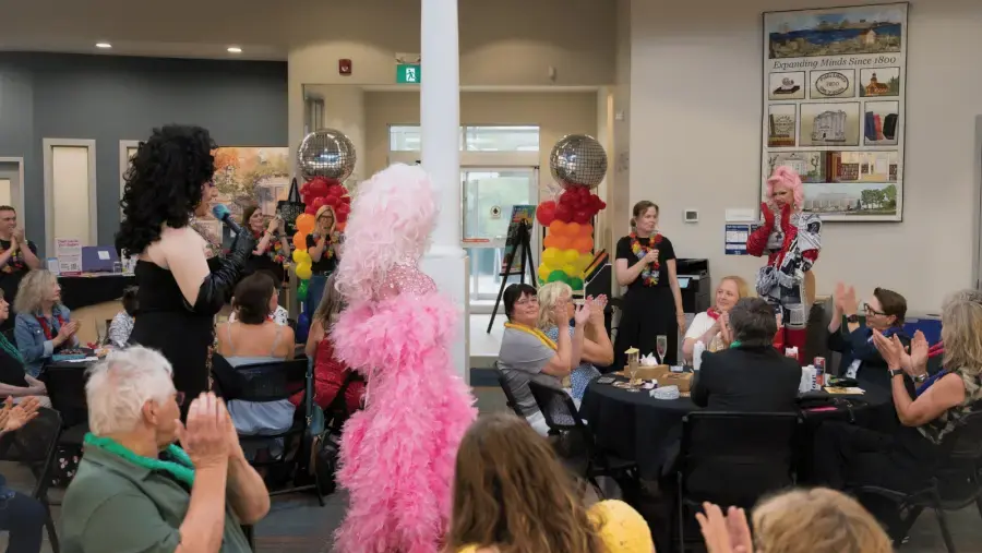 Seated attendees applaud as drag performers and library staff give a thank you message.