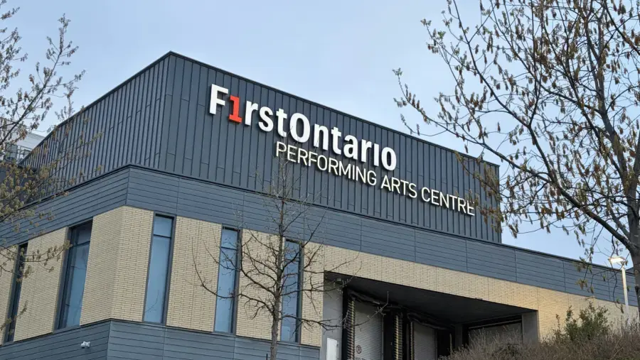 Exterior view of the FirstOntario Performing Arts Centre building, featuring the venue’s name prominently displayed on the façade, with trees framing the entrance.