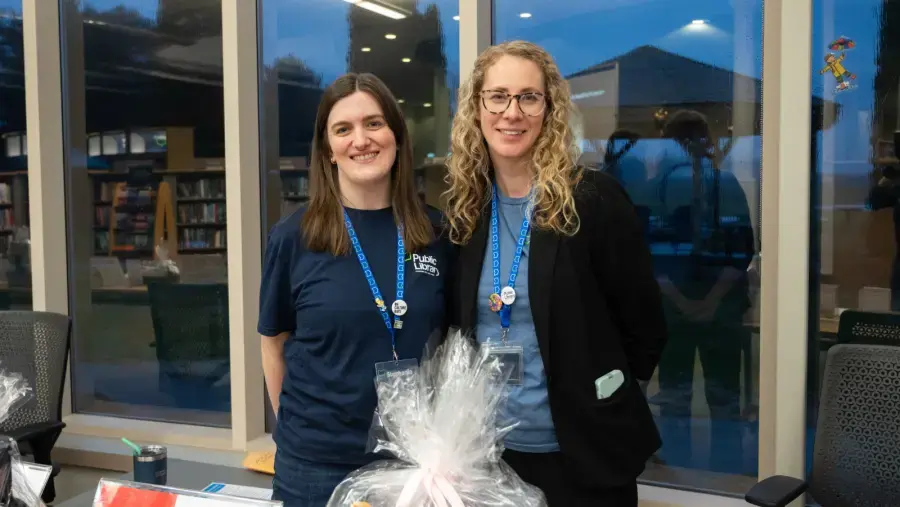 Library staff, Stephanie and Lexie pose for a photo at the silent auction table.