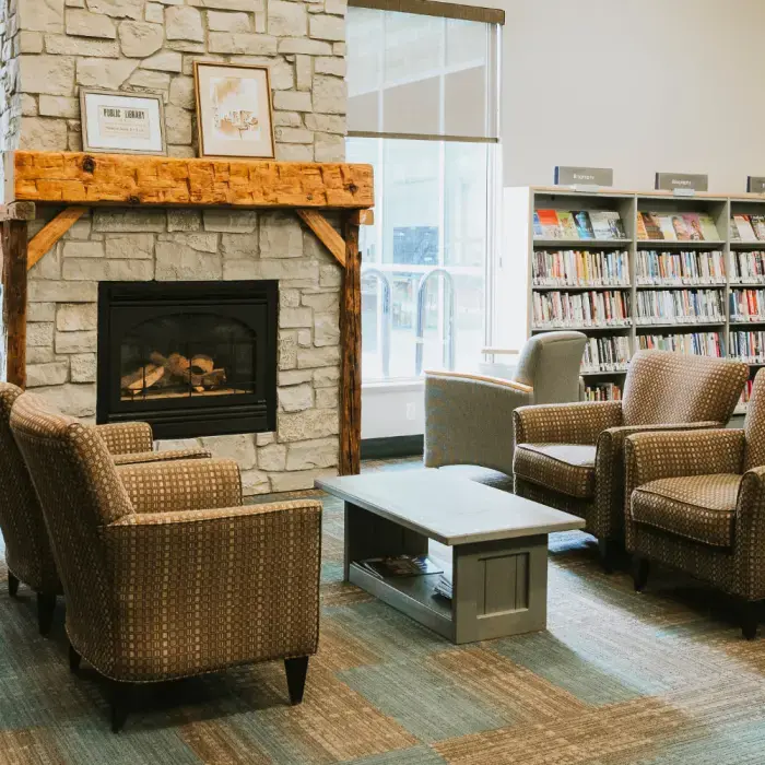 A seating area in the NOTL Library. There is a fireplace and mantel made of stone and reclaimed wood. In front of the fireplace is a coffee table with four cozy chairs surrounding the table.