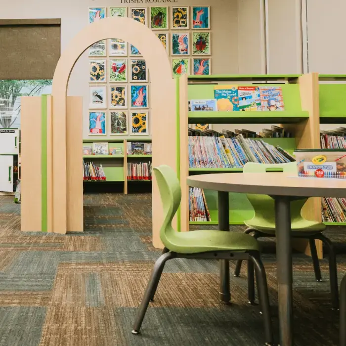 A photo of the NOTL Library children's picture book section. The bookshelves are highlighted by a lime green tone and there is an arched door feature leading to an enclosed area. In the foreground are a child-sized table and chairs in lime green.