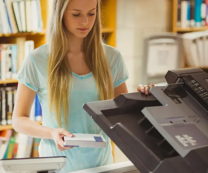 Image features a young woman with blond hair and a light blue shirt standing at a photocopier making copies.